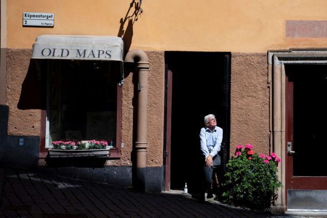 A shop owner enjoys the sun outside his empty shop, in Gamla stan, the old town in central Stockholm